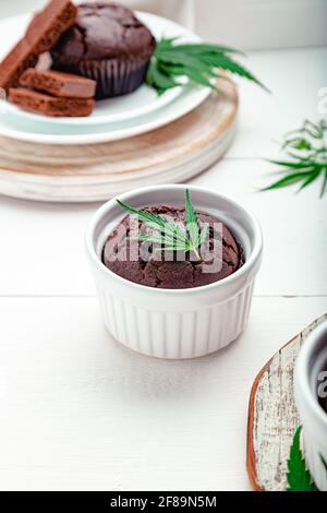 Cucinando i muffin alle erbacce in una teglia da forno con la cannabis sulla parte superiore del tavolo bianco. Muffin alla torta al cioccolato con foglie di cannabis e erbacce cbd. Medico Foto Stock