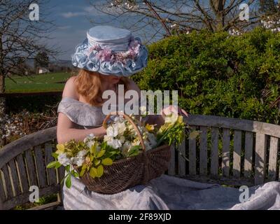 Giovane donna seduta sulla panchina sulla piattaforma di osservazione vestita nel cofano pasquale con abito a spalle scoperte. Il campo verde nel backdround. Foto Stock