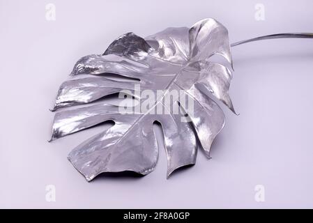 Grande foglia di Monstera dipinta in argento su sfondo grigio. Concetto di lusso minimalista. Ottimo per poster decorazione interni. Foto Stock