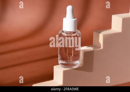 Bottiglia cosmetica in vetro mock up sul podio scala. Acido ialuronico, prodotto per la cura della pelle del siero su piedistallo beige. Foto Stock