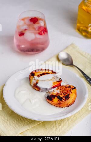 Servite pesche cotte al forno con miele e panna pesante montata Su piatto bianco e bicchiere di cocktail Raspberry Foto Stock