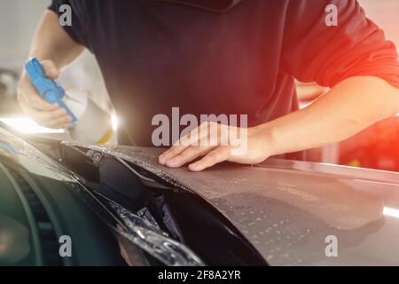 Il lavoratore Detailer spruzza con sapone sid e avvolge PPF o pellicola protettiva per auto sul cofano del veicolo. Foto Stock