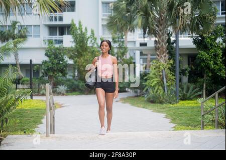 Ritratto di una giovane donna afroamericana nel camminare con tappetino yoga Foto Stock