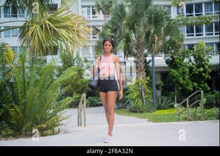 Ritratto di una giovane donna afroamericana nel camminare con tappetino yoga Foto Stock