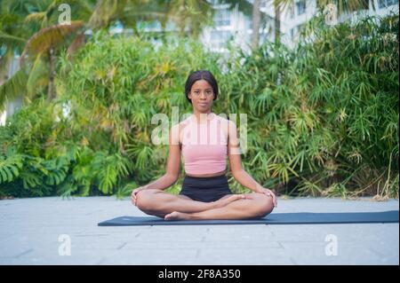 Ritratto di una giovane donna afroamericana che stretching nello Yoga Posa all'aperto durante il giorno con sfondo verde tropicale Foto Stock