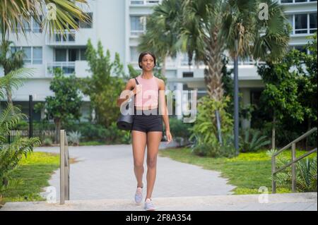 Ritratto di una giovane donna afroamericana nel camminare con tappetino yoga Foto Stock