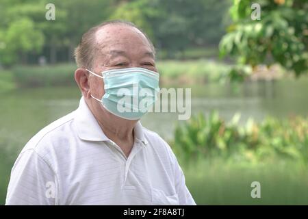 Uomo asiatico anziano che indossa la maschera facciale nel parco. Primo piano. Foto Stock