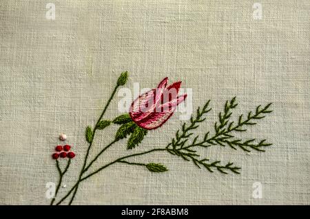 Ramoscello ricamato con un bocciolo di rose rosse, ramoscello di conifere e piccole bacche rosse su un tessuto di cotone bianco. Foto Stock
