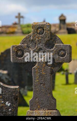 Croce celtica scolpita in pietra contro l'erba verde e il cielo blu A Graveyard in Irlanda Foto Stock