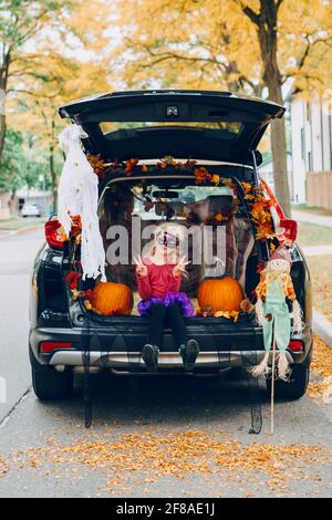 Trucco o tronco. Bambina che celebra Halloween in tronco di auto. Capretto con le zucche rosse che celebrano le feste tradizionali di ottobre all'aperto. Distan sociale Foto Stock