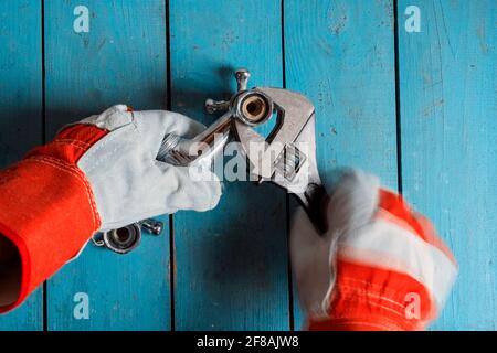 Impianti idraulici di lavoro. La ricerca guasti viene eseguita su un vecchio tavolo di legno blu (blu fantasma). Un lavoratore guanto gira un rubinetto di acqua fredda. Eliminando così Th Foto Stock