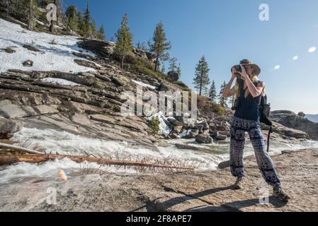 Una fotografa femminile si prende un momento per scattare una foto lungo un tratto panoramico di fiume e montagne nel parco nazionale di Yosemite, California. Foto Stock