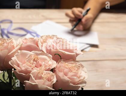 Sposa ragazza firma inviti a nozze, in primo piano delicato rosa bouquet di rosa da sposo Foto Stock