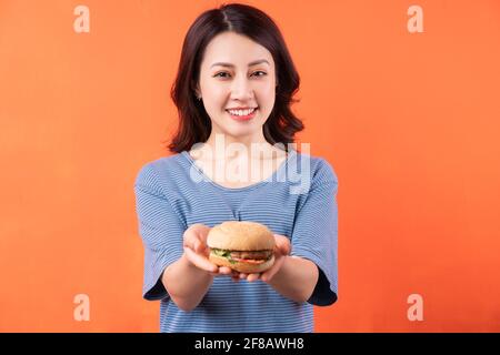 Giovane donna asiatica che tiene hamburger su sfondo arancione Foto Stock