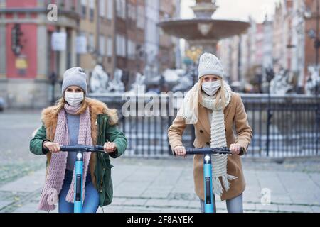 Amici di ragazza che indossano maschere di fronte e che si spostano su scooter dentro la città Foto Stock