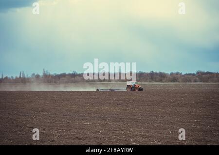 Il trattore agricolo aratura il campo e si prepara alla semina Foto Stock