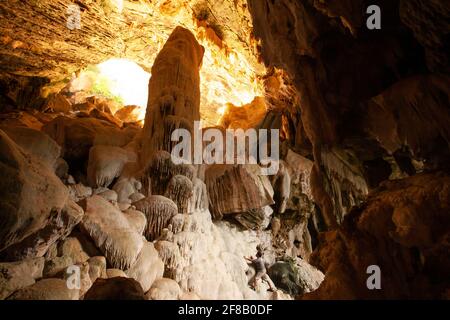 Un giovane che stende il grande complesso di grotte a Koh Wua Ta Lap nel Golfo della Thailandia. Il fascio di sole splende sulla grotta. Foto Stock