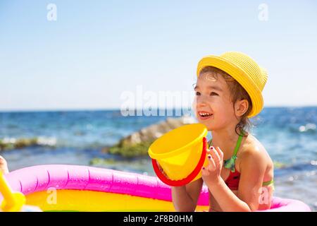 Ragazza in giallo cappello di paglia gioca con il vento, l'acqua e un  distributore d'acqua in una piscina gonfiabile sulla spiaggia. Prodotti  indelebili per proteggere i bambini Foto stock - Alamy