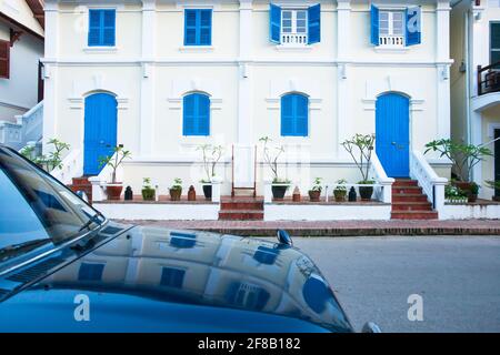 Pittoreschi edifici coloniali sulla strada di Luang Prabang, Laos, porte blu vintage e finestre di un edificio coloniale si riflettono su un'auto blu. Foto Stock