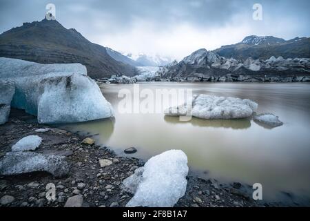 Ghiaccio che galleggia nelle acque fangose del lago glaciale con ghiacciaio sullo sfondo in una giornata nuvolosa e piovosa. Fjallsarlon, Islanda. Foto Stock