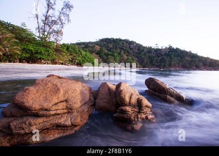 Antiche pietre rocciose sulla spiaggia tropicale al tramonto. Le morbide onde dell'oceano si infrangono sulle rocce. Isola di Koh Chang, Ranong, Thailandia. Foto Stock