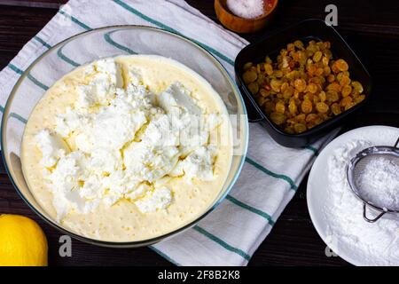 Ciotola di vetro con pastella e formaggio casereccio fatto in casa. Il processo di fabbricazione della pasta di cagliata. Pasta per frittelle di formaggio cottage. Foto Stock