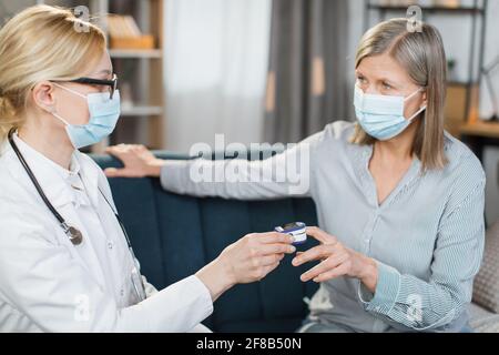 Primo piano di operatrice sanitaria femminile, medico o infermiere, utilizzando pulsossimetro a dito, mentre si visita paziente malato anziana donna a casa, controllando il livello di ossigenazione. Foto Stock