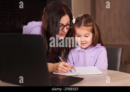 Madre che aiuta sua figlia durante il suo lavoro. Formazione online a distanza Foto Stock