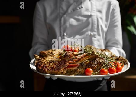 Giovane agnello appena cotto per le vacanze di Pasqua, servito dal piatto del cameriere. BBQ Agnello e un letto di rosmarino Foto Stock