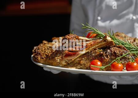 Agnello al barbecue e un letto di rosmarino, agnello giovane appena cotto per le vacanze di Pasqua, servito dal piatto del cameriere Foto Stock