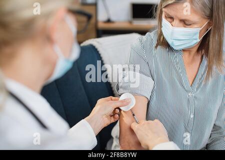 Vaccinazione, iniezione di insulina. Medico professionale altamente qualificato che fa l'iniezione di insulina alla donna diabetica di mezza età durante la sua visita a casa. Foto Stock