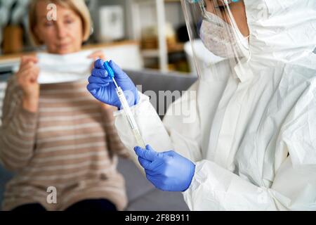 Operatore medico in guanti di protezione e indumenti da lavoro che tengono la provetta Foto Stock