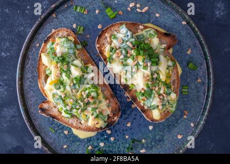 Delizioso pane tostato con insalata di aglio verde, uova bollite e panna acida sul piatto, primo piano Foto Stock