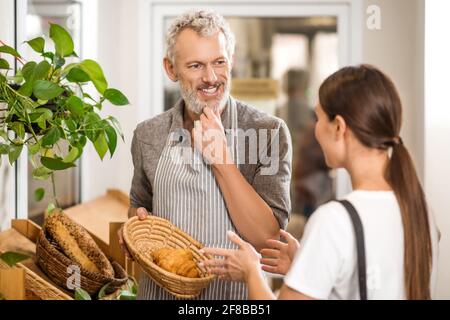 Uomo in grembiule che mostra croissant al cliente Foto Stock