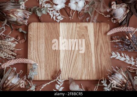 Composizione con fiori selvatici secchi, pikelet, fiori di protea e un elemento in legno al centro. Foto Stock