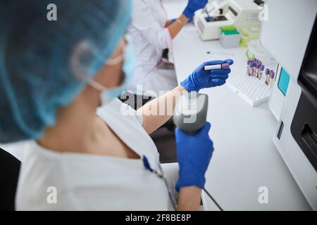 Biochemista femminile che scansiona il campione di sangue vacutainer Foto Stock