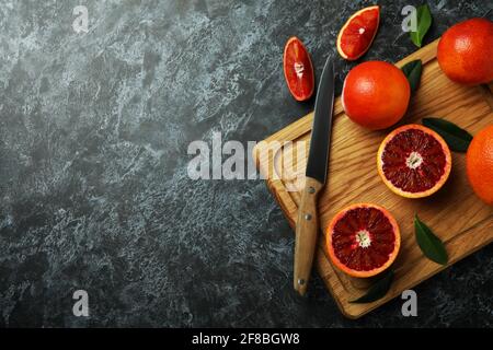 Tavola con arance rosse, foglie e coltello su tavola nera fumosa Foto Stock