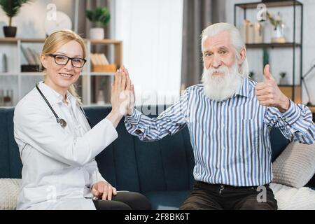 Bell'uomo anziano sopportato, mostrando il pollice fino alla macchina fotografica, soddisfatto dopo la conversazione riuscita e dando alto cinque al suo medico gp di famiglia, visitandolo a casa. Foto Stock