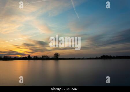 Splendido tramonto su un lago ghiacciato con alberi sulla riva, vista invernale Foto Stock