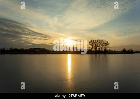 Tramonto su un lago ghiacciato con alberi sulla riva, vista invernale Foto Stock