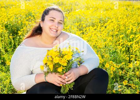 bella ragazza più-size posa all'aperto con un bouquet di camomili. Donna Chubby in un prato con margherite Foto Stock