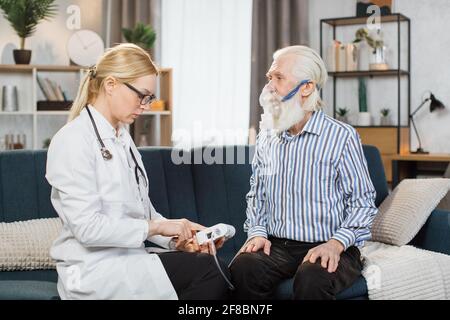 Trattamento dell'asma per i pazienti anziani geriatrici. Donna caucasica medico medico generico aiutare il suo paziente anziano per fare l'inalazione con nebulizzatore, durante la visita a casa. Foto Stock