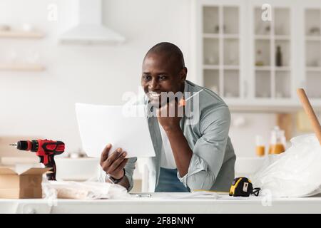 Buon uomo nero che legge le istruzioni di installazione, tenendo il cacciavite nell'interno della cucina Foto Stock