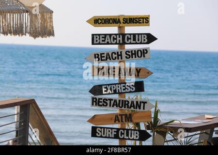 Indicazione di direzione sullo sfondo del mare. Puntatore in legno sulla spiaggia, Surf club, Shop, ATM. Foto Stock