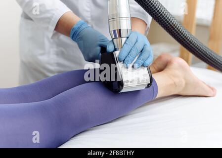 Beautician fa il massaggio del polpaccio del GPL delle gambe alla donna giovane in vestito viola. Massaggio linfodrenante. Trattamenti dimagranti. Foto Stock