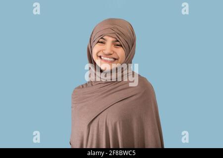 Ritratto di ragazza teen musulmana positiva in hijab sorridente a. fotocamera su sfondo blu dello studio Foto Stock