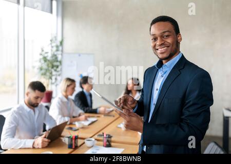 Uomo d'affari africano allegro che utilizza Tablet computer in piedi in ufficio moderno Foto Stock