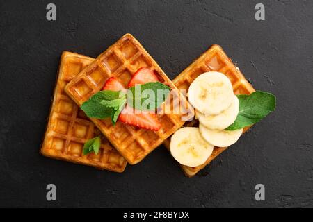 Waffle belgi con fragola, banana e menta su fondo di pietra nera