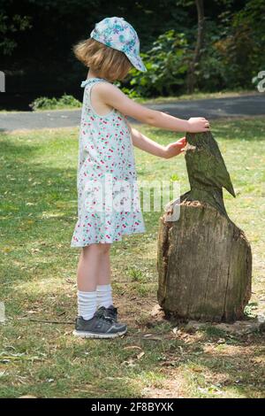 Giovane bambina di 5 anni di età con una scultura di gufo ( o uccello simile ) realizzata con un ceppo di alberi scolpiti in un parco pubblico. REGNO UNITO. (120) Foto Stock