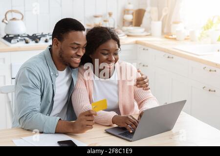 Famiglia Africana che paga le fatture di utilità a casa con il laptop e. Carta di credito Foto Stock